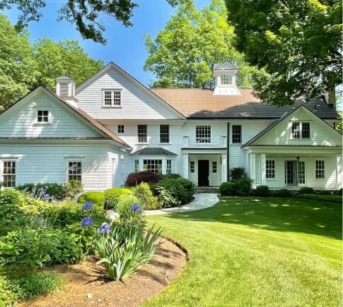 A large white house with a garden in the front yard.