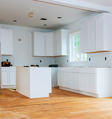 A kitchen with white cabinets and wood floors.
