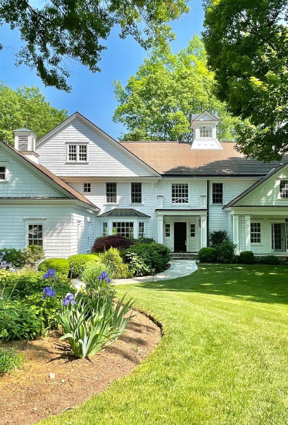 A large white house with a garden in the front yard.